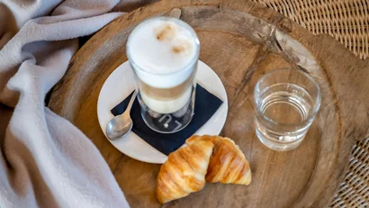 Latte Macchiato, Croissant und Glas Wasser auf Holztablett mit Seezeit Lodge Decke