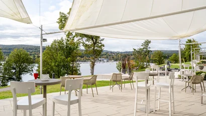 Outdoor-Sitzbereich mit weißen Stühlen und Blick auf See und grüne Hügel