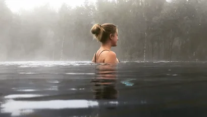 Frau entspannt im Wasser mit nebligem Wald im Hintergrund