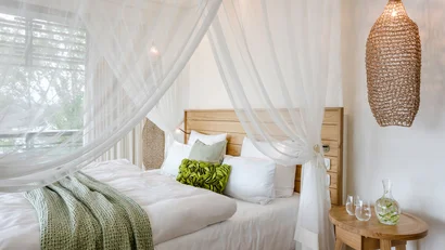 Helles Schlafzimmer mit Himmelbett, grünen Kissen und Holztisch mit Wasserkrug