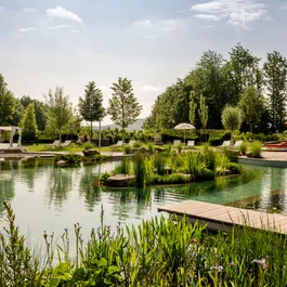 Natürlicher Schwimmteich mit Liegestühlen, Pavillons und grüner Landschaft