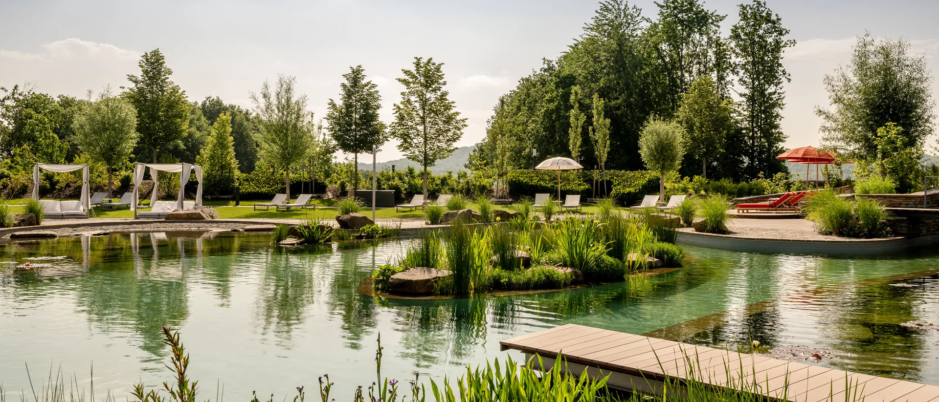Natürlicher Schwimmteich mit Liegestühlen, Pavillons und grüner Landschaft