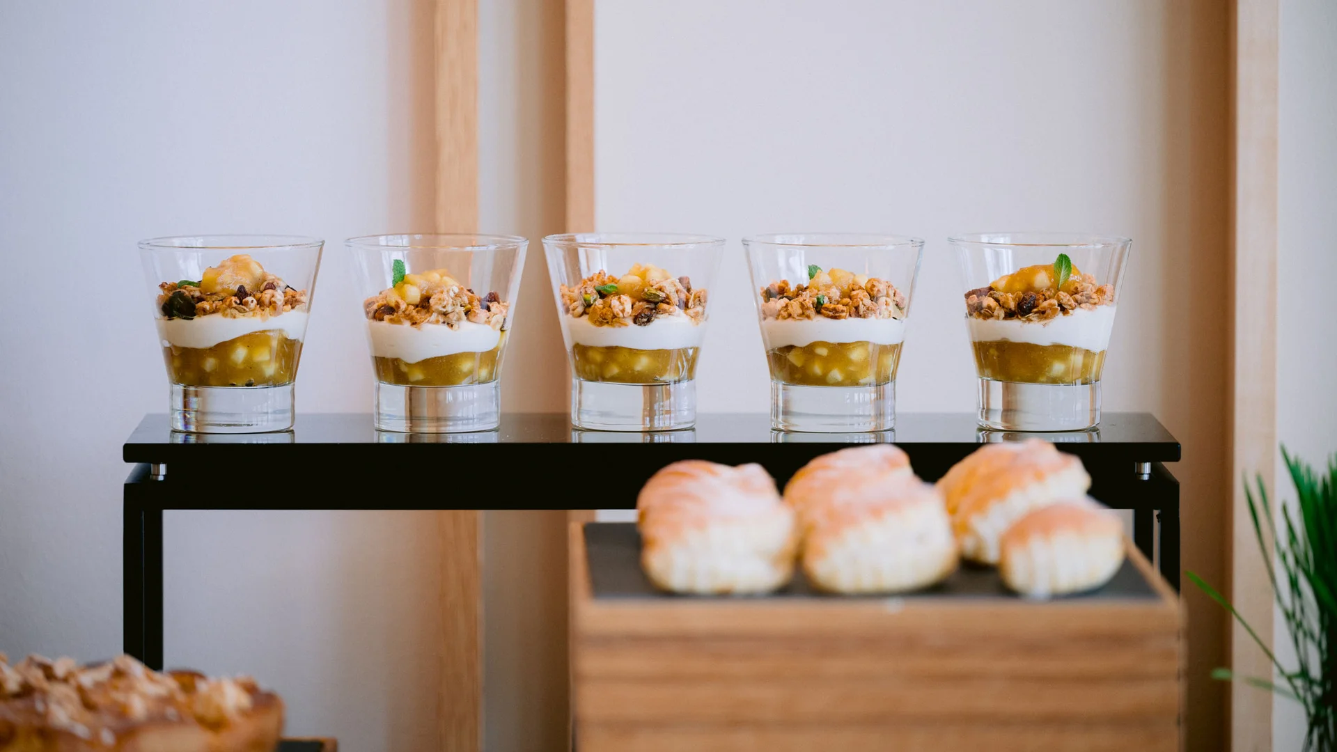 Fünf Gläser mit Joghurt, Früchten und Müsli auf einem schwarzen Tisch