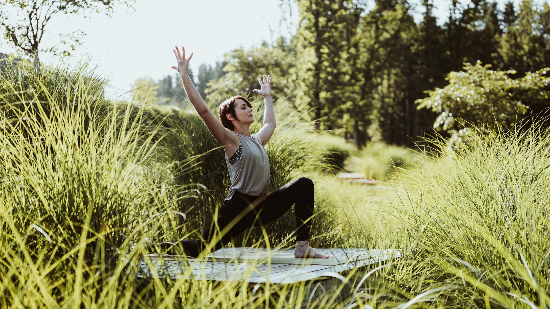 Woman practicing yoga outdoors on mat surrounded by green plants
