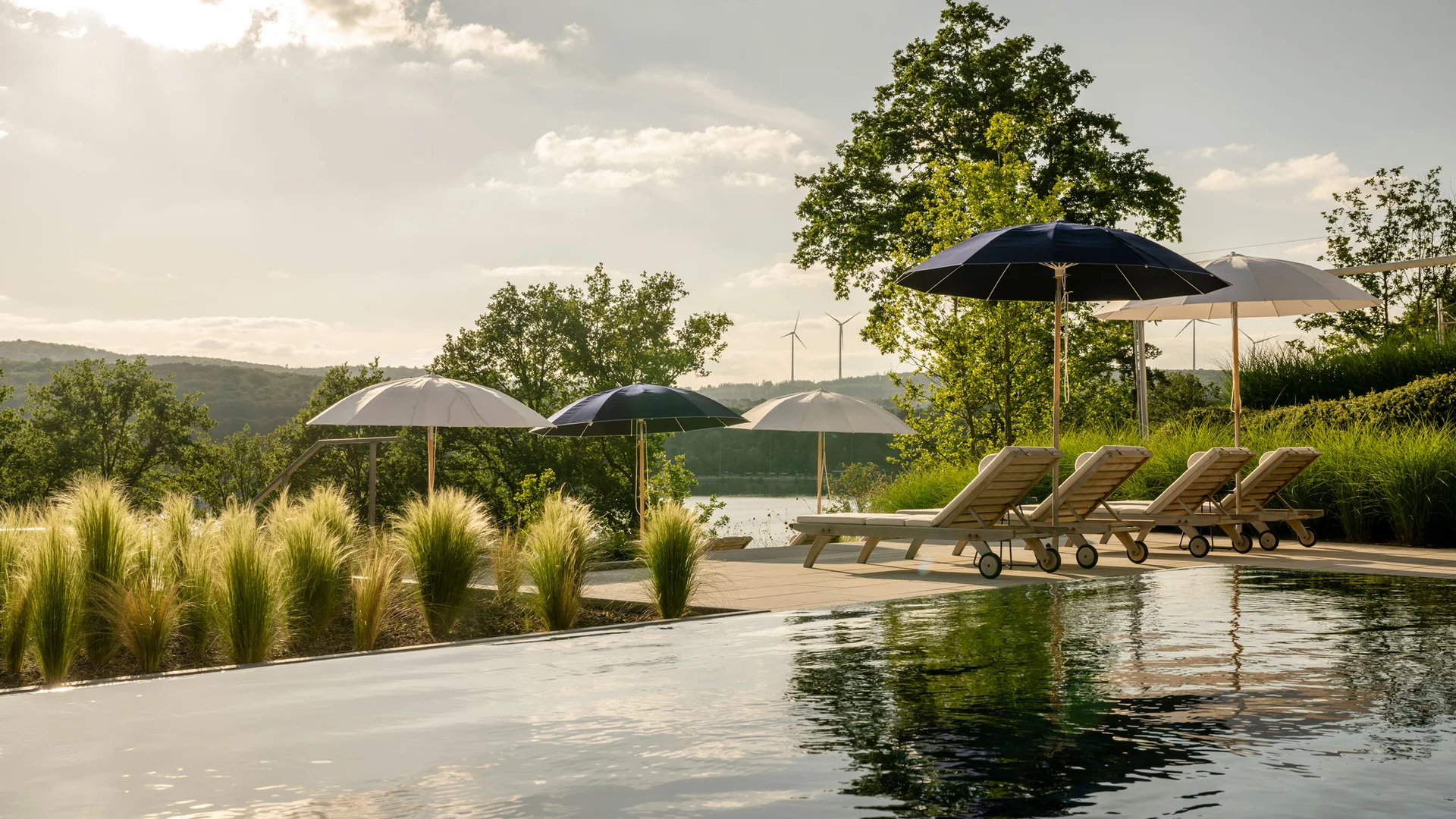 Pool mit Liegestühlen und Sonnenschirmen in grüner Landschaft bei Sonnenuntergang