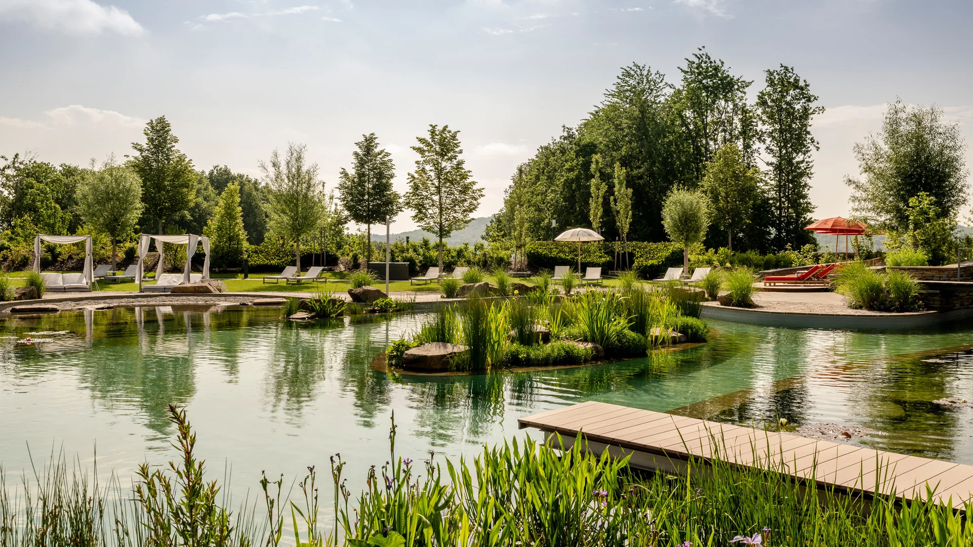 Natürlicher Schwimmteich mit Liegestühlen, Pavillons und grüner Landschaft