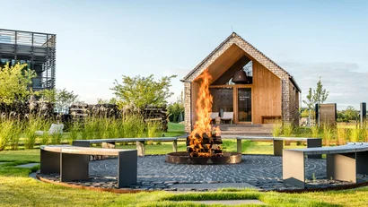 Offene Feuerstelle mit Flammen vor einer kleinen Holzhütte im Garten