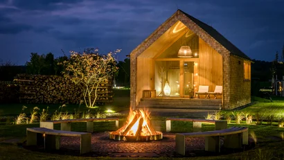 Beleuchtete Holzhütte mit Feuerstelle und Sitzbänken im Garten bei Nacht