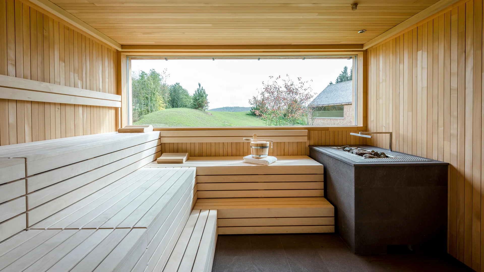 Innenraum einer Sauna mit Holzbänken und großer Landschaftsfensterfront