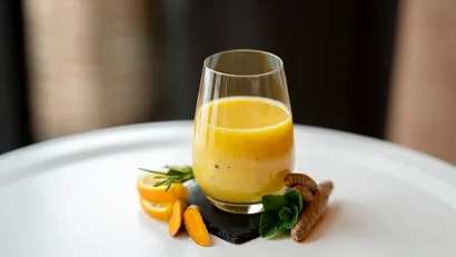 Glas mit frischem Kurkuma-Saft und Kurkumastücken auf weißer Oberfläche