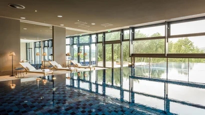 Moderner Innenpool mit Liegestühlen und großen Fenstern mit Blick ins Grüne