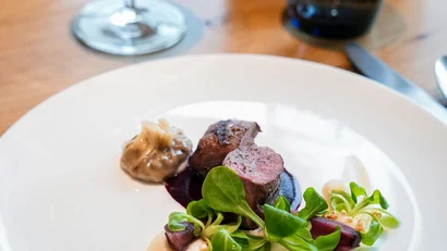 Fein angerichtetes Gericht mit Fleisch, Sauce und Salat auf weißem Teller