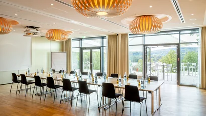 Moderner Konferenzraum mit U-förmigen Tischen und Blick auf Terrasse und Natur