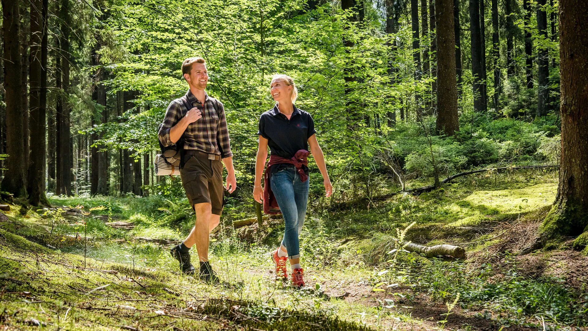 A couple happily hiking through a sunlit green forest