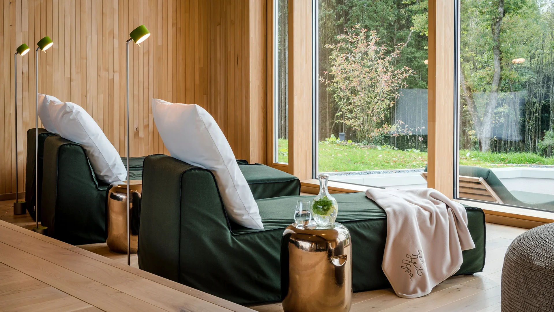 Entspannungsbereich mit Liegen, Kissen und Wasser in einem modernen Holzinterieur