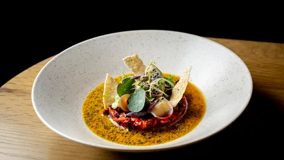 Kreativ angerichtetes Gourmetgericht mit Sauce und frischen Kräutern in weißer Schüssel