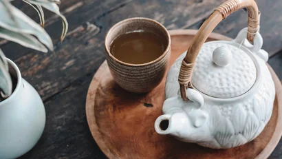 Weißer Teekessel und Tasse Tee auf einem Holztablett auf Holztisch