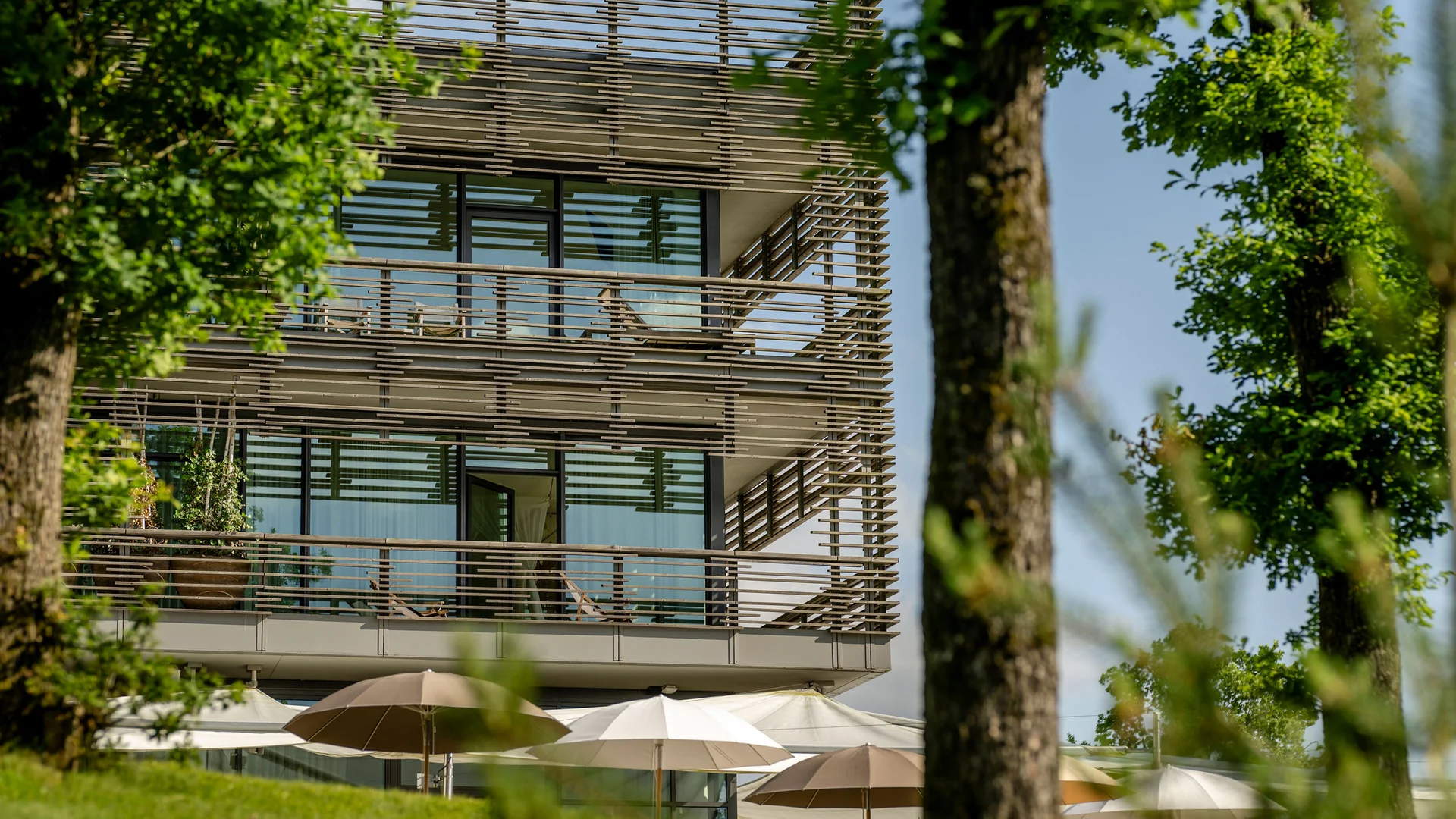 Modernes mehrstöckiges Gebäude mit Balkonen und Sonnenschirmen in einem grünen Garten