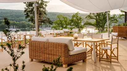 Outdoor-Lounge mit Korbsessel und Tischen mit Blick auf See und Wald