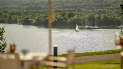 Segelboot auf funkelndem See mit grünem Wald im Hintergrund