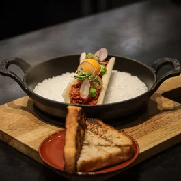 Gourmetgericht mit rohem Ei und geröstetem Brot auf Holztisch