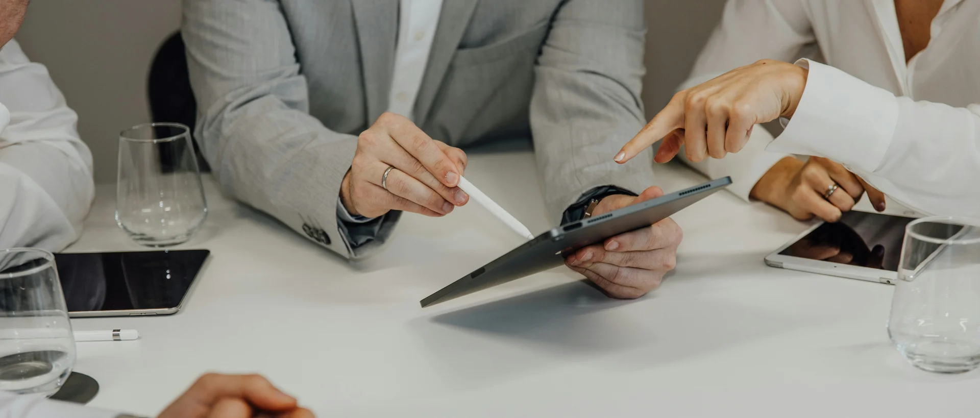 Personen in formeller Kleidung zeigen auf Tablet bei Besprechung