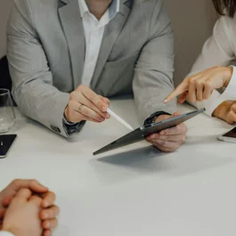 Personen in formeller Kleidung zeigen auf Tablet bei Besprechung