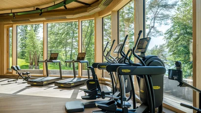 Heller Fitnessraum mit Technogym-Geräten und großen Fenstern mit Naturblick
