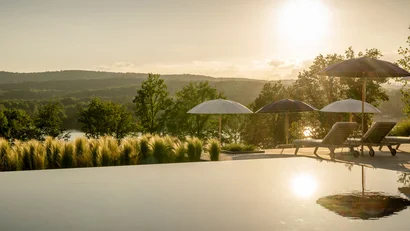 Sonnenuntergang über Pool mit Liegestühlen und Sonnenschirmen vor grüner Landschaft