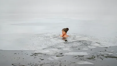Frau schwimmt im eisigen Wasser mit zerbrochenem Eis um sie herum.