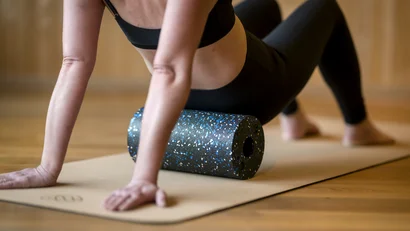 Frau bei Selbstmassage mit Faszienrolle auf Yogamatte
