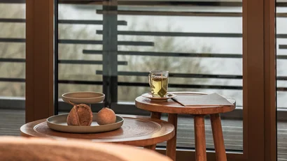 Blick durch Fenstertür auf Balkon mit Tisch, Glas Tee und Brötchen