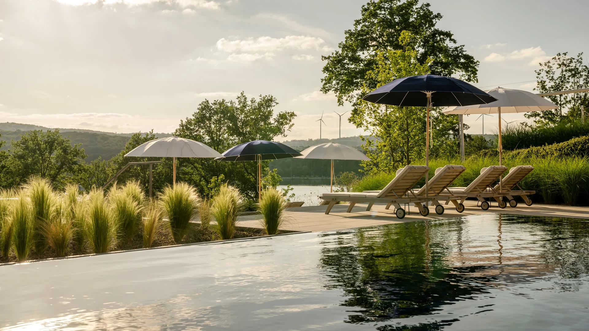 Pool mit Liegestühlen und Sonnenschirmen in grüner Landschaft bei Sonnenuntergang