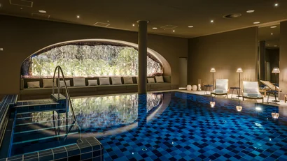 Indoor-Schwimmbad mit blauen Fliesen, Sitzbereich und großen Fenstern mit Wasserfall